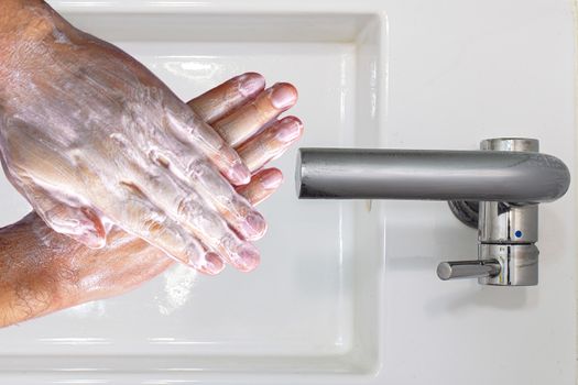 Top view of a person washing hands with soap on a wash basin