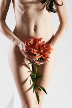 Intimate part of a woman's body with flower in hands. Close up of a woman body with flower on her pubes. No retouch.