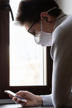 A young man in a medical mask looks at the phone screen for information on how to protect yourself from the coronavirus
