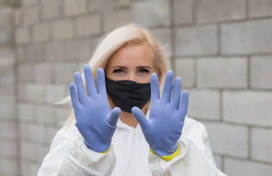 Woman in black mask, white protective suit and gloves making sigh stop