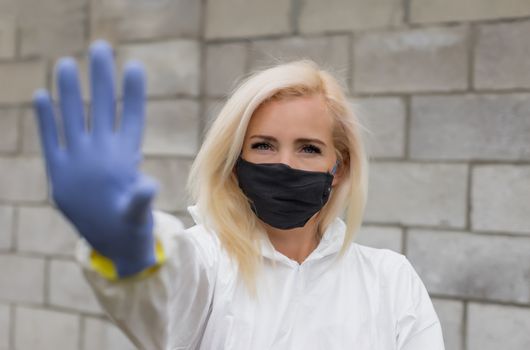 Woman in mask, white protective suit and gloves making sigh stop