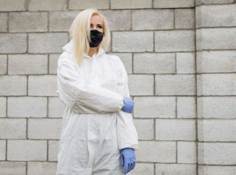 Woman in mask, white protective suit and gloves outdoors