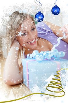 Cheerful blond woman holding a present lying on the floor against snow falling