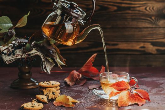 Pour hot tea in glass cup. Autumn teatime composition on dark ba