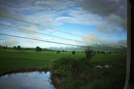 View from train window in motion of countryside and sky on sunny warm , in Thailand , 