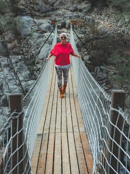 Adult woman standing on a hanging wooden bridge in the nature.