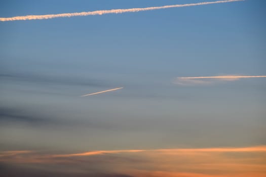 Contrail from airplane on a blue sky against a sunset.