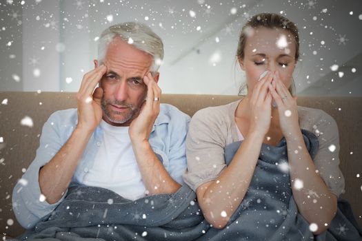 Composite image of sick couple sitting on the couch under a blanket