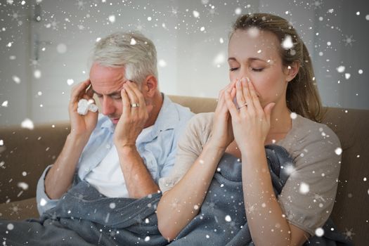 Composite image of sick couple sitting on the couch under a blanket