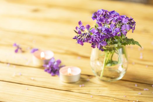 Violet flowers in glass jar and perfumed candle on natural wood 