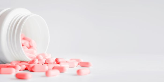 Pink pills with spilled out of a plastic jar. Medicine capsules on white background with copy space.