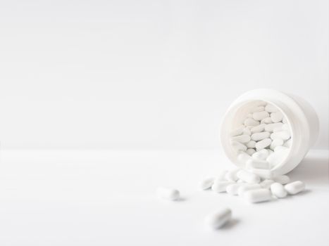 White pills spilled out of a plastic jar. Medicine capsules on w