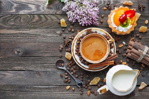 Rustic wooden background with cup of coffee, milk, fruit tart and lilac flowers. White vintage dinnerware and spoon. Breakfast at summer morning. Top view, place for text.