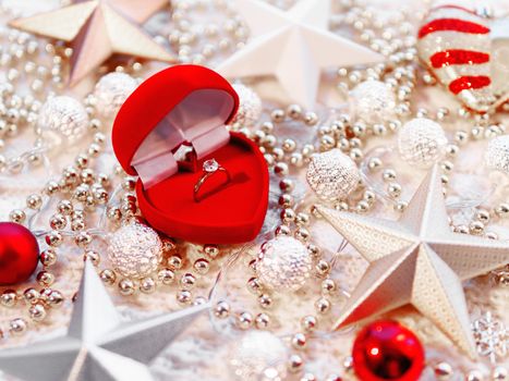 Christmas and New Year star decorations on white knitted background. Red heart gift box with engagement golden ring, metal light bulbs with delicate pattern, beads.