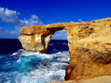 Cliff rock bridge with waves crashing on it during a sunny day (azure window in Malta). Brigde collapsed in early 2017 due to severe weather conditions