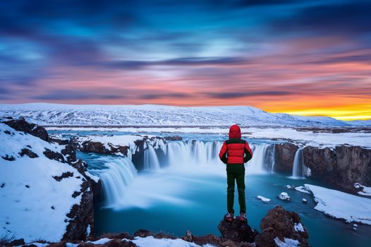 Godafoss waterfall at sunset in winter, Iceland. Guy in red jacket looks at Godafoss waterfall.
