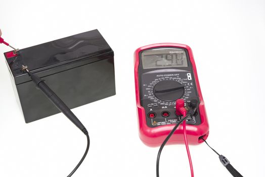 Multimeter instrument measuring battery voltage over a white background
