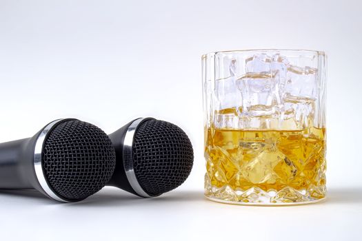 A whisky glass with ice and liquor and two karaoke microphones on a white background