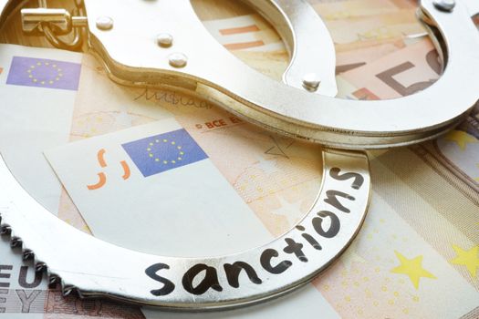 Euro bills and handcuffs with word sanctions. Economical restrictive measures.