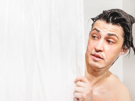 Young man in soap suds looks out from behind a curtain in the bathroom. Man was taking a shower.