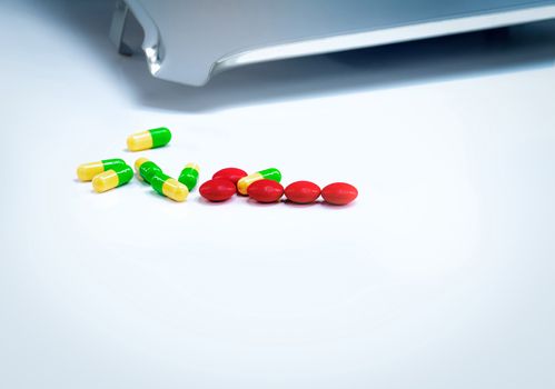 Red tablets and green-yellow capsules pills with drug tray on wh