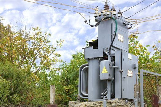 Transformer substation stands in the middle of the garden against a blue cloudy sky.