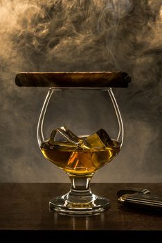 Smoking Cuban Cigar on Top of Elegant Whisky Glass with Ice Cubes. Copy Space Background.