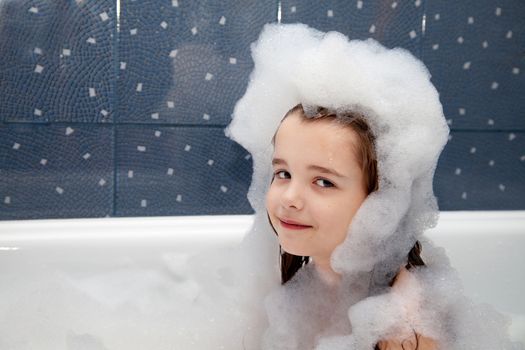 little girl sitting in a bath with soap suds