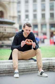 Beautiful young man holding pretzel and relaxing in park