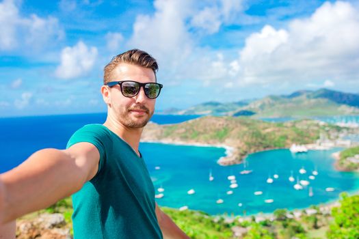 Young man taking selfie with view of English Harbor from Shirley Heights, Antigua, paradise bay at tropical island in the Caribbean Sea