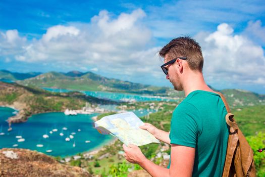 Young tourist man with map background of English Harbor from Shirley Heights, Antigua, paradise bay at tropical island in the Caribbean Sea