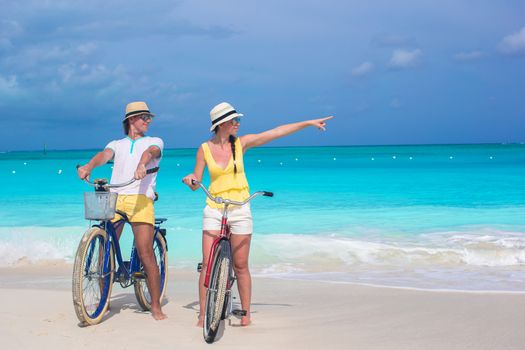 Young happy couple riding bikes on white tropical beach
