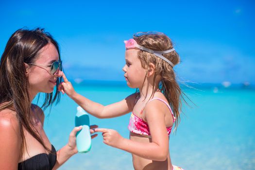 Little girl applying sunblock cream on her mom nose