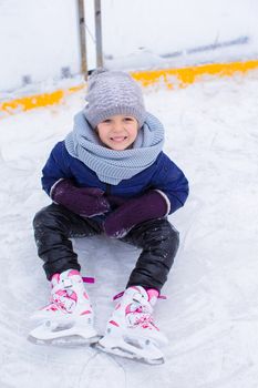 Little adorable girl sitting on ice with skates after fall