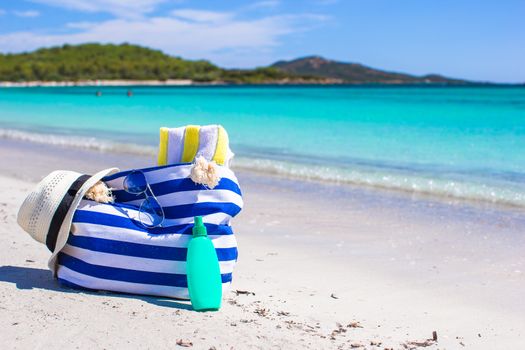 Stripe bag, straw hat, sunblock and towel on beach