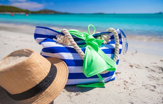 Stripe bag, straw hat, sunblock and towel on white tropical beach
