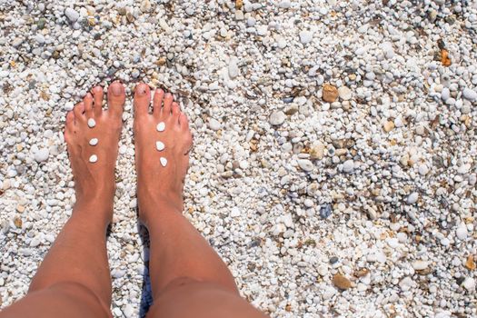 Female legs with pebbles on white sandy beach