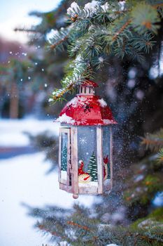 Christmas lantern with snowfall hanging on a fir branch