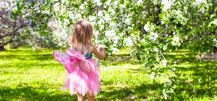 Adorable little girl in blossoming apple tree garden at may