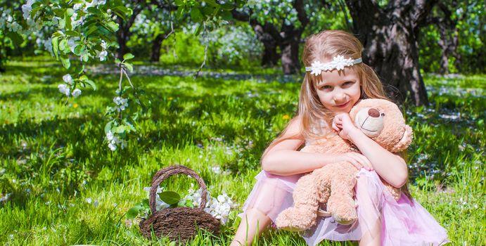Adorable little girl in blossoming apple tree garden at may