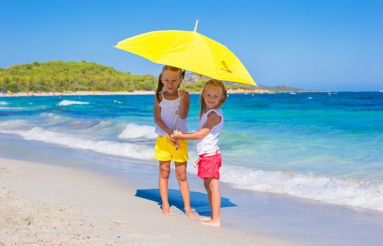 Little girls with big yellow umbrella during tropical beach vacation