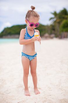 Little adorable girl in swimsuit with suntan lotion bottle