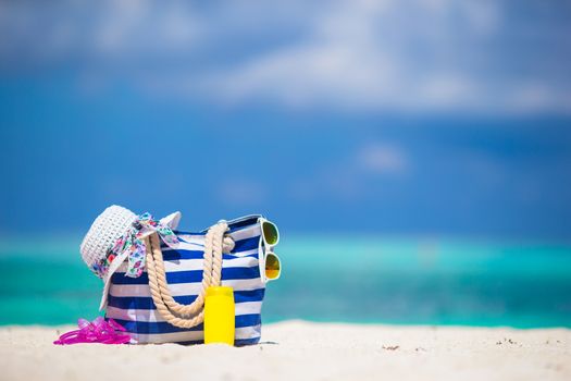 Blue bag, straw white hat, sunglasses, flip flop and sunscreen bottle on tropical beach