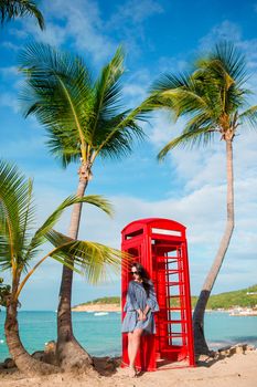Beautiftul woman near red phone booth in Dickenson's bay Antigua. Beautiful landscape with a classic phone booth on the white sandy beach in Antigua