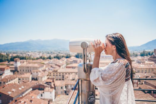 Girl looking at coin operated binocular on terrace at small town in Tuscany
