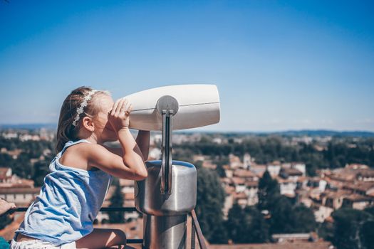 Beautiful girl looking at coin operated binocular on terrace at small town in Tuscany