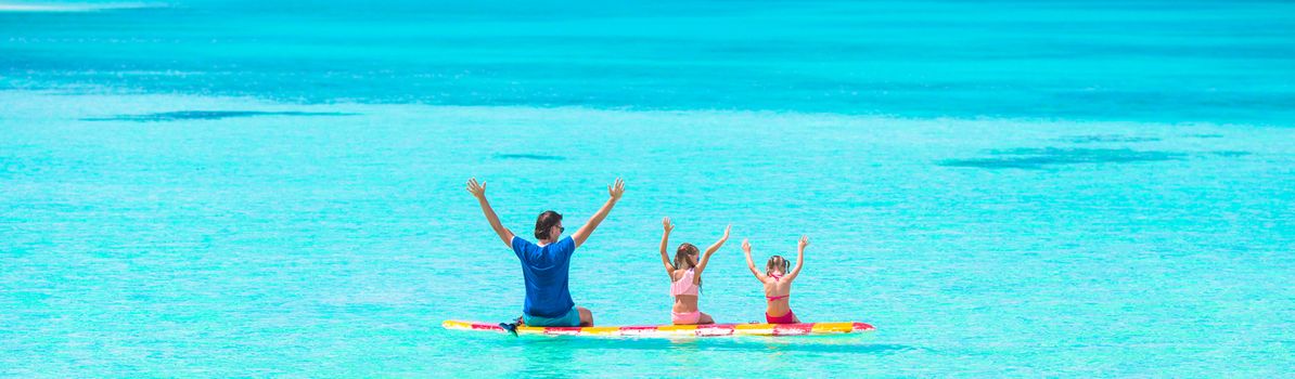Little girls with father swimming on a surfboard in the turquoise sea