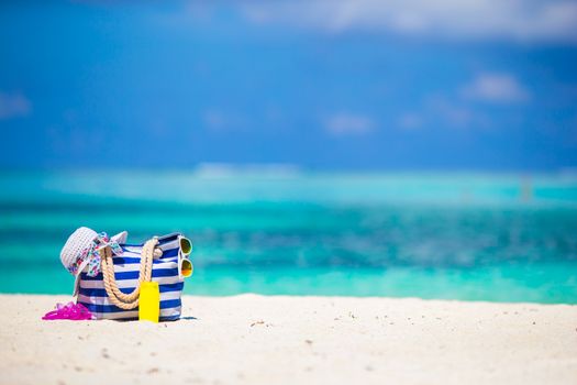 Stripe bag, blue towel, sunglasses, sunscreen bottle and swimsuit on white beach