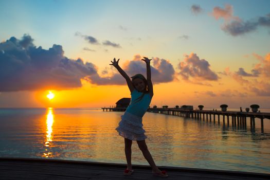Silhouette of adorable little girl on wooden jetty at sunset