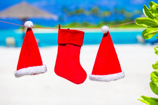 Red Santa hats and Christmas stocking hanging on tropical beach